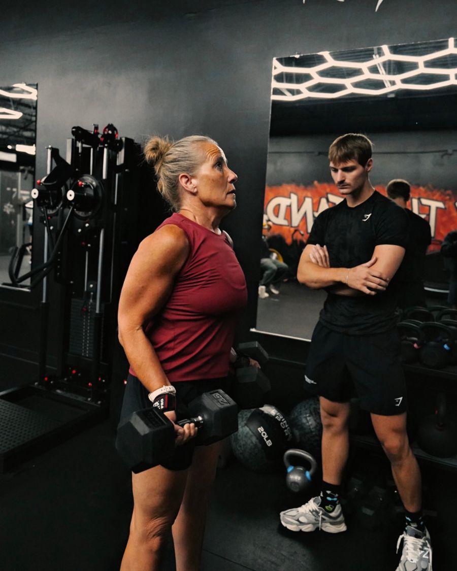 Client lifting dumbbells while her coach watches her form